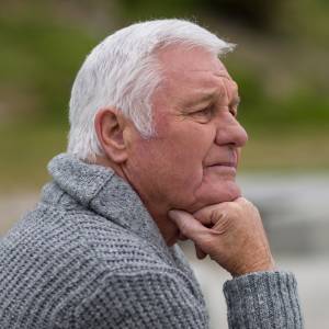 White-haired man sitting on the steps near beach in a contemplative pose.