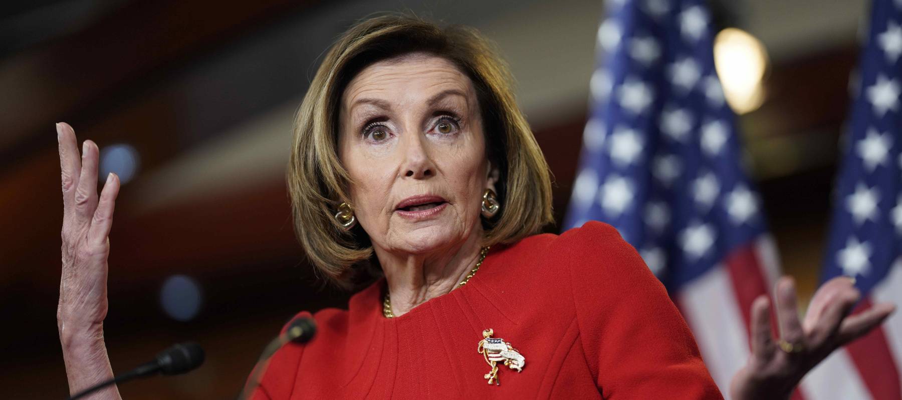 Nancy Pelosi stands at a podium with her hands up