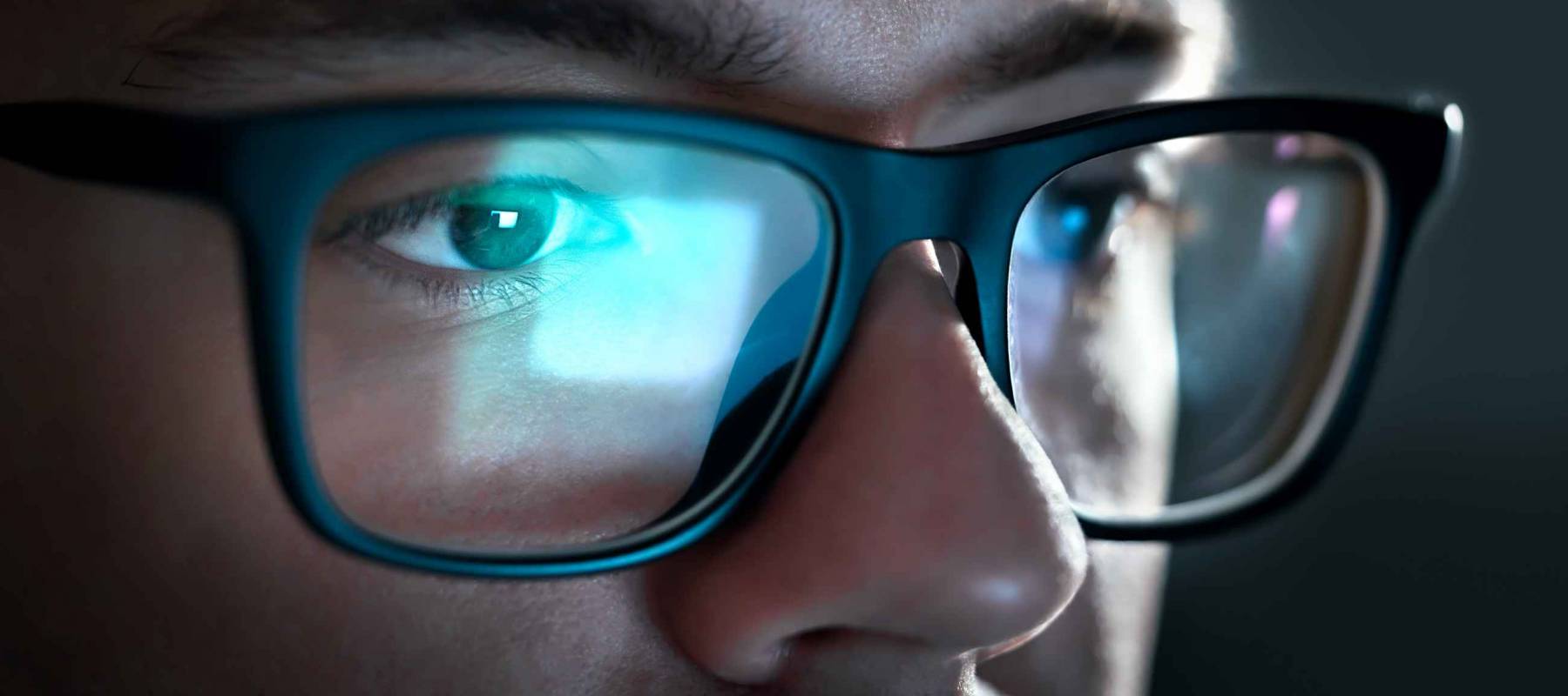 Computer screen light reflect from glasses. Close up of eyes. Business man, coder or programmer working late at night with laptop. Thoughtful focused guy in dark. Reflection of monitor.