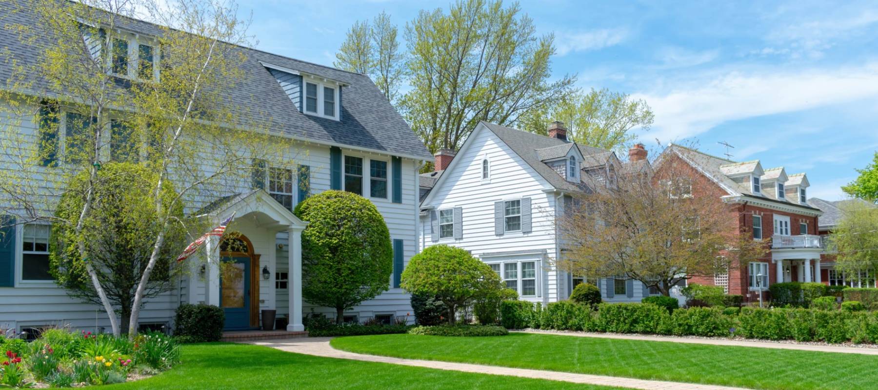 Row of traditional suburban homes with lush green front lawns in nice residential neighborhood.
