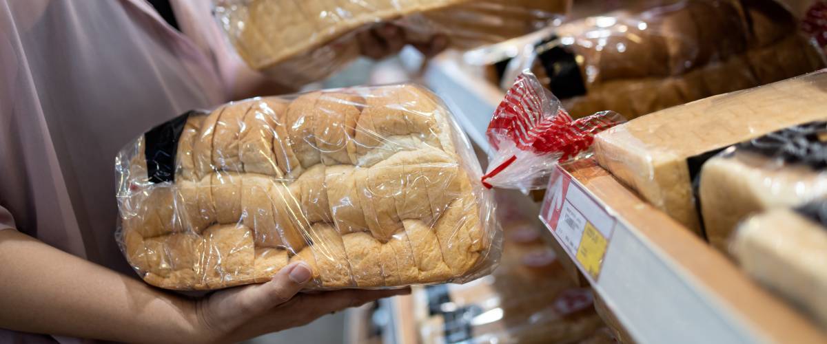 Person shopping at grocery store holding two loaves of bread