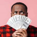 Portrait of a confused african man wearing shirt standing isolated, showing money banknotes