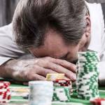 It is not my day. Depressed senior man in shirt and suspenders leaning his head at the poker table with money and gambling chips laying all around him
