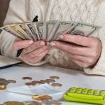 Woman in a white sweater handles money with a calculator nearby.