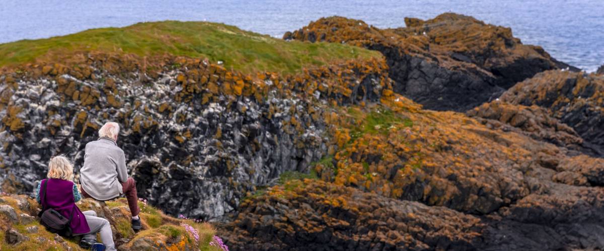 Rear view of senior couple admiring the stunning coastline at Carrick-a-Rede Island, after crossing the famous rope bridge in County Antrim, Northern Ireland.