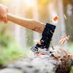 Lumberjack in checkered shirt chops tree in deep forest with sharp ax, Detail of axe, wood chips fly around.
