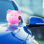 Closeup image new car with piggy bank, key on hood isolated outside corporate building.