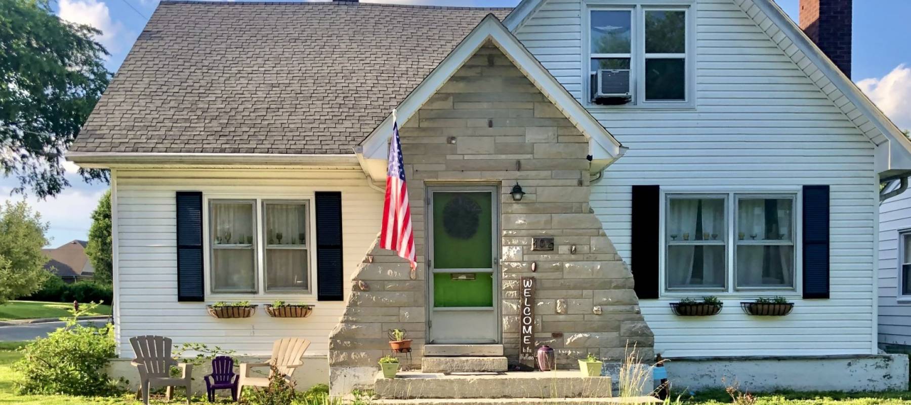 Beautiful white cottage on a perfect summer day; blue sky with fluffy clouds, American flag on house.