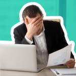 Stressed unhappy young businessman in office in front of laptop, holding financial document and facepalming