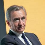 Bernard Arnault makes a cheeky face to the camera in front of a yellow backdrop.