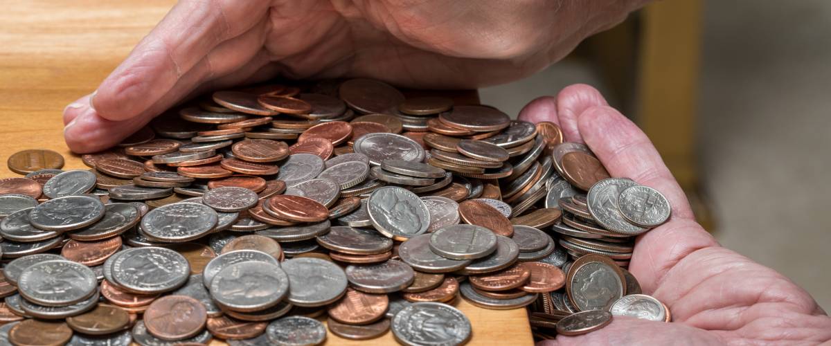 Hundreds of US coins being gathered into hands on wooden table as concept for hoarding during shortage of loose change
