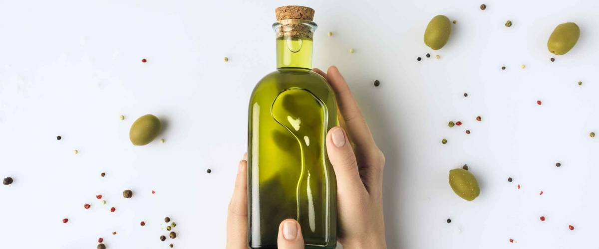 Cropped image of woman holding glass bottle of olive oil in hands isolated on white