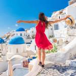 Europe travel vacation fun summer woman dancing in freedom with arms up happy in Oia, Santorini, Greece island. Carefree girl tourist in European destination wearing red fashion dress.