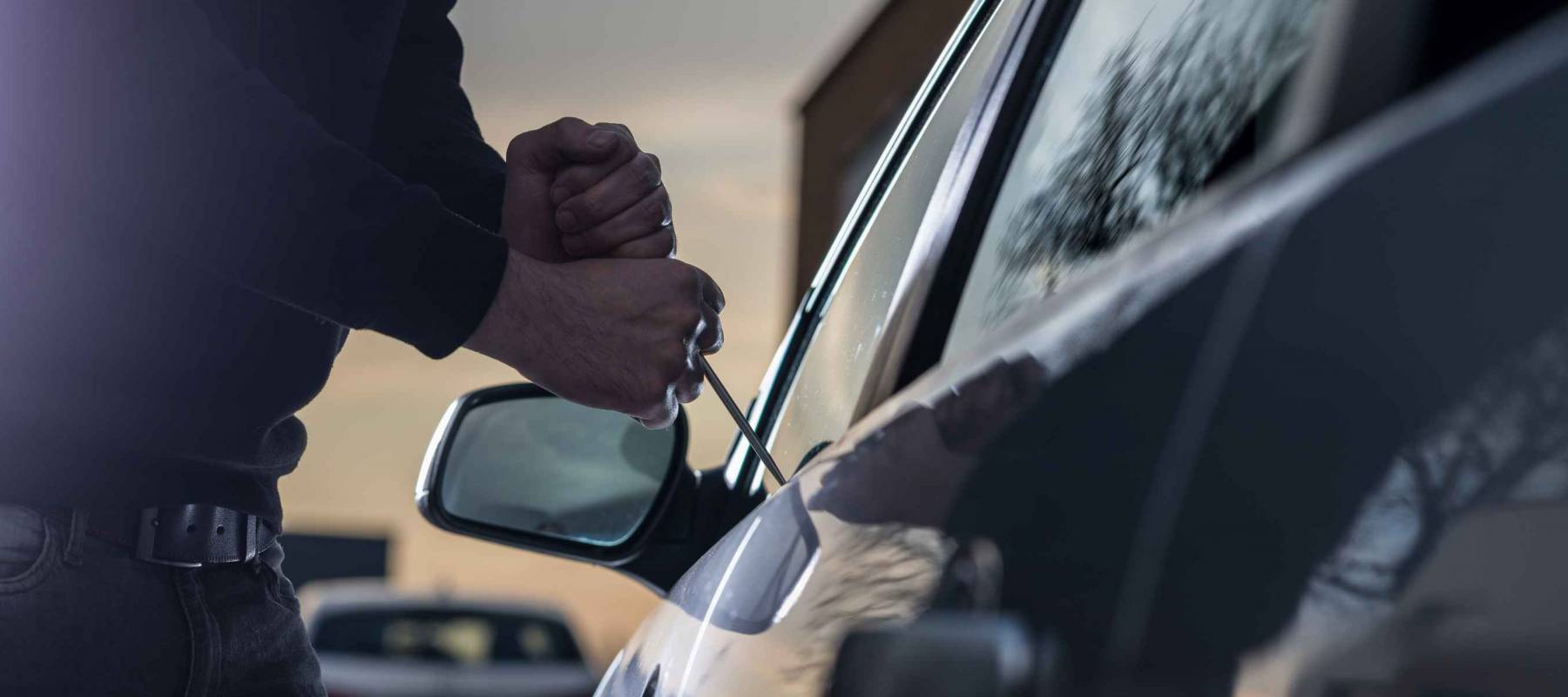 Auto thief in black balaclava trying to break into car with screwdriver. Car thief, car theft