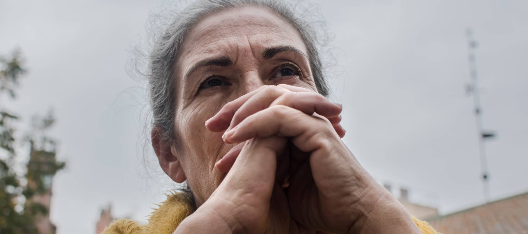 Close up of woman looking seriously off into the distance with hands clasped in front of mouth.