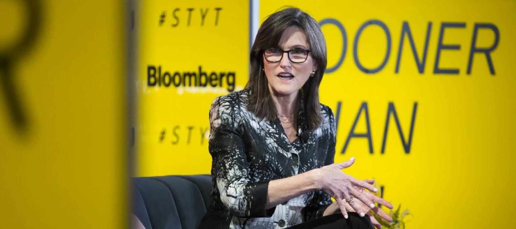 Cathie Wood sits on a stage talking expresively.