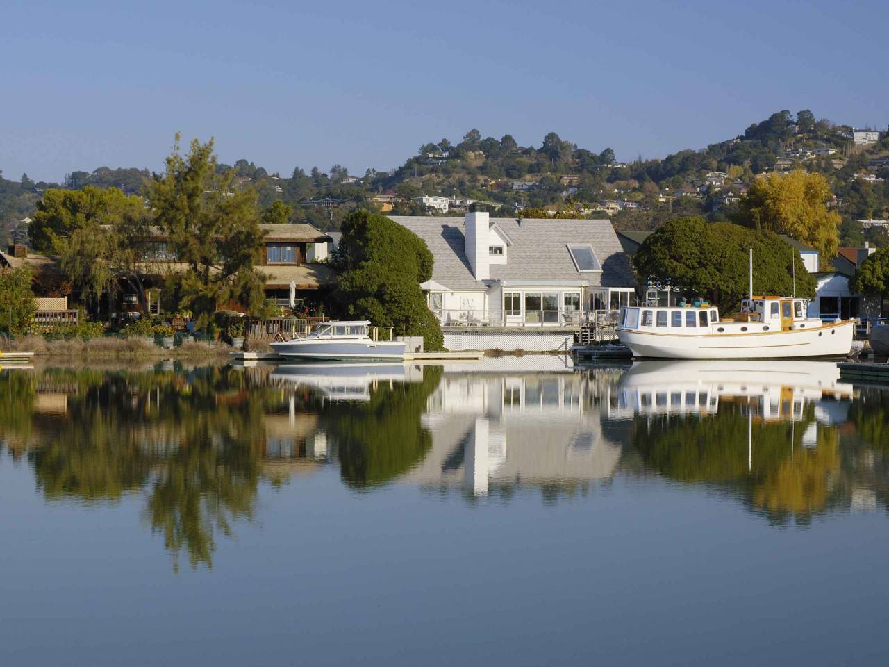 Nice houses with boats are reflected in calm waters of Corte Madera Creek in Larkspur, California.