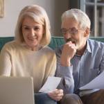 Happy older couple holding documents and looking at computer screen