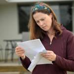 A woman reads a letter in her front yard with a concerned look on her face