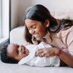 A young mom tickling her laughing baby's tummy