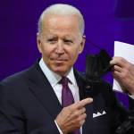 U.S. President Joe Biden removing his mask and pointing to a piece of paper in his hand