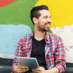 Young latin man using a tablet at the street.
