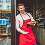 Portrait of happy professional confectioner holding plate with sweet biscuit desserts working at bakery shop