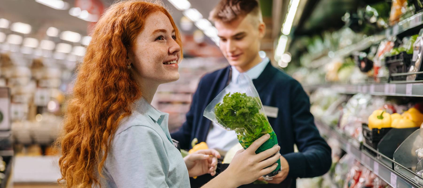 Male and female workers packing fresh produce on the shelves in supermarket. Grocery store employees working in produce section.