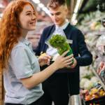 Male and female workers packing fresh produce on the shelves in supermarket. Grocery store employees working in produce section.