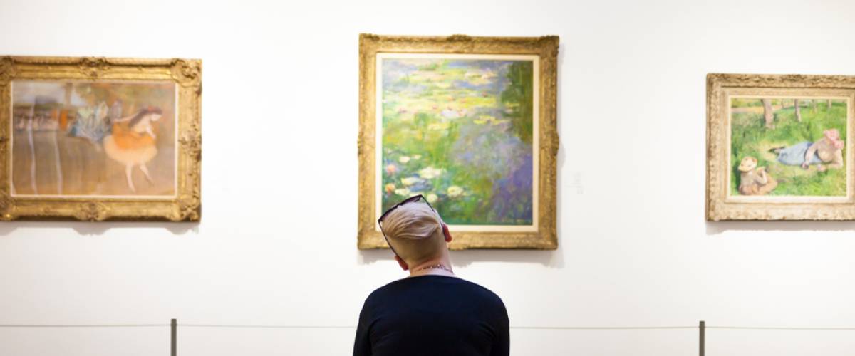 A woman is sitting on a bench looking at the painting by Claude Monet of water lilies