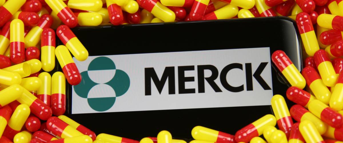 Close up of mobile phone screen with logo lettering of Merck pharmaceutical company on pile yellow red drug capsules