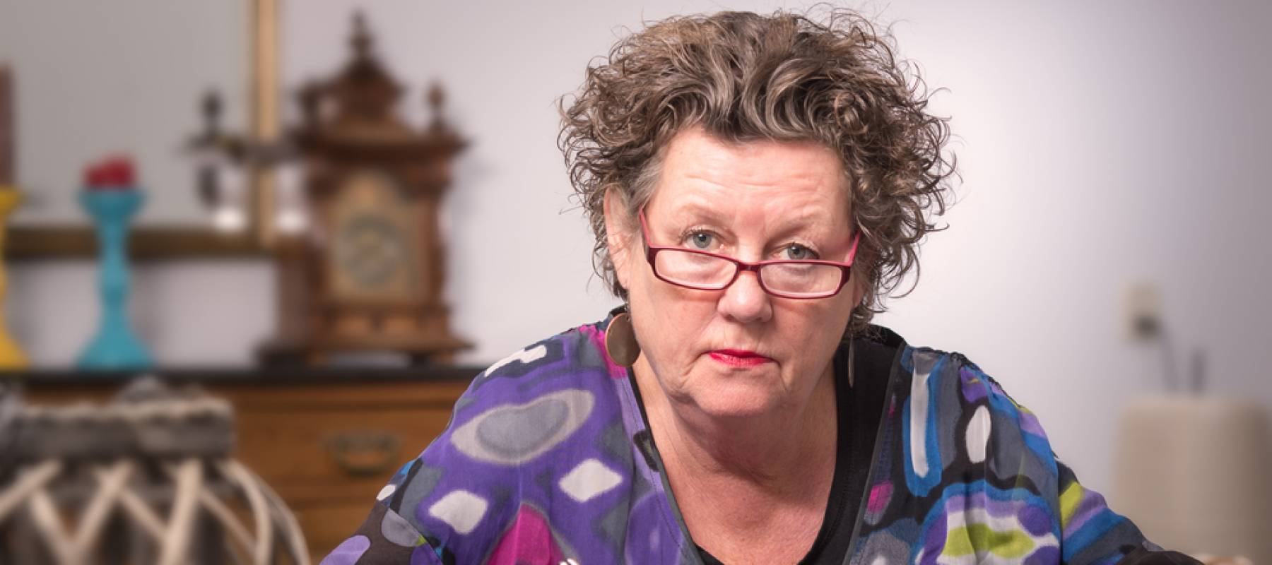 An older woman peering over her glasses at the camera with a look of disdain