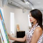 Young caucasian woman standing in an art gallery in front of painting displayed on white wall