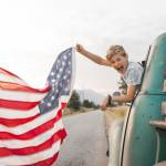 Boy waving American flag out of an old truck