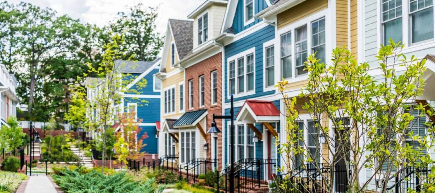 Row of colorful, red, yellow, blue, white, green painted residential townhouses, homes, houses with brick patio gardens in summer