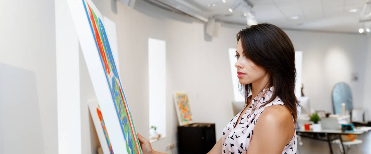 Young caucasian woman standing in an art gallery in front of painting displayed on white wall