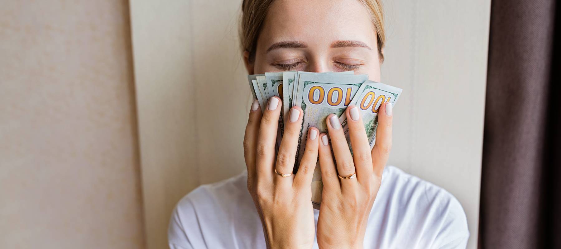 Young Caucasian woman sniffing cash money one hundred dollars bills with closed eyes