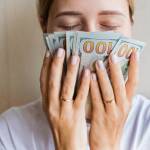 Young Caucasian woman sniffing cash money one hundred dollars bills with closed eyes