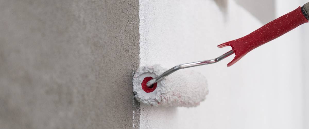 Paint roller being used with white paint on a gray wall