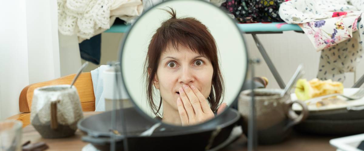 Woman looks at self in mirror shocked by cluttered room and stress
