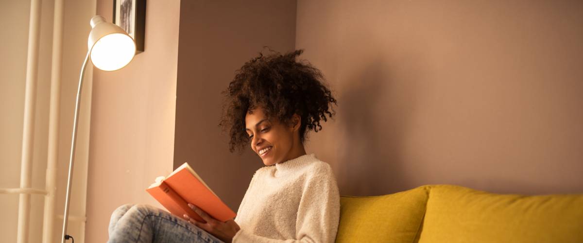 Woman sitting on couch under a lamp, reading