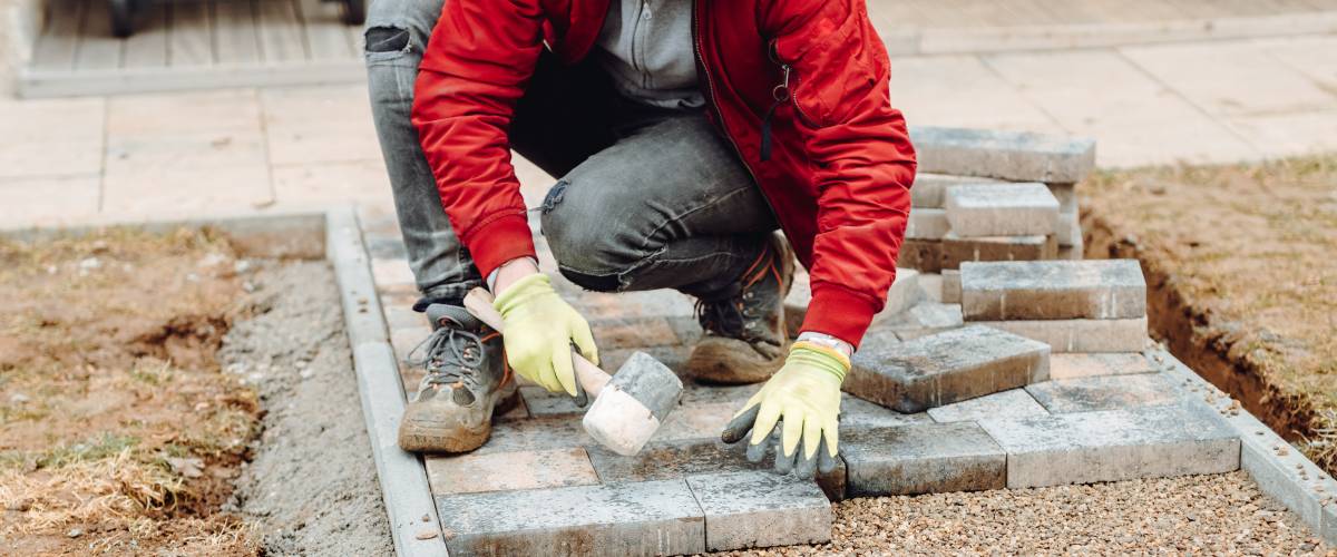 body of a man in a red jacket kneeling to work on paving stones