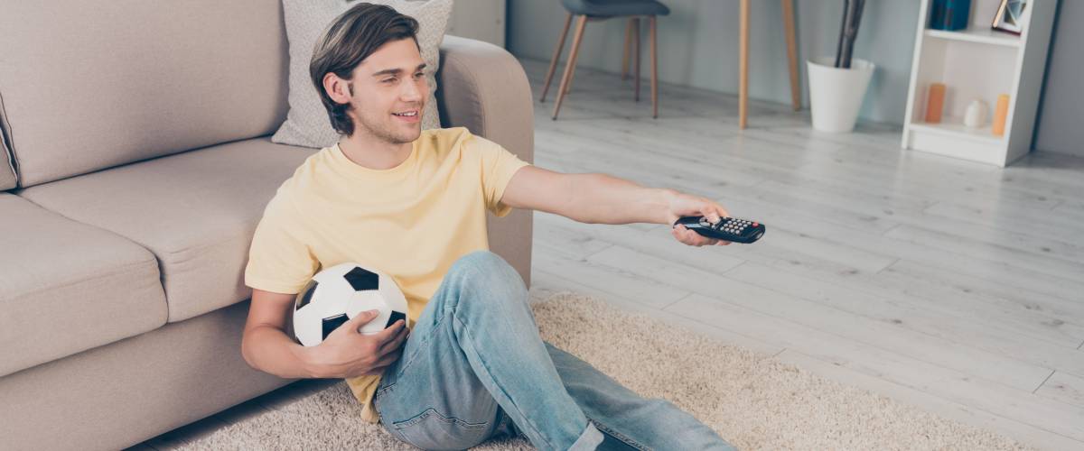 Man holding soccer ball, sitting in front of the TV with his shoes on