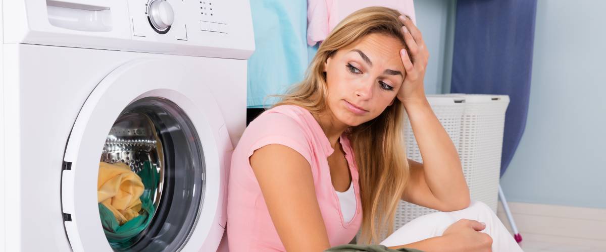 Woman sitting against clothes dryer, looking frustrated