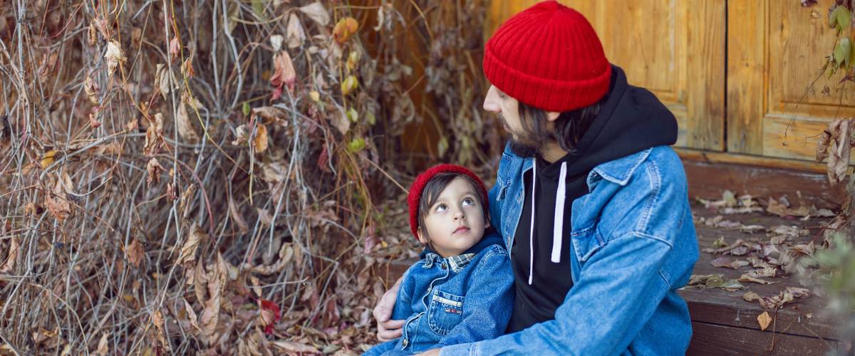 a man in a red beanie with his son sitting on the steps which are covered in brown vines