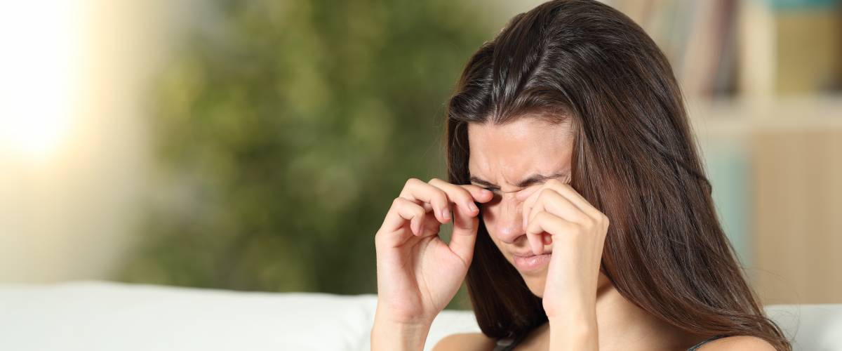 Woman sitting on couch, rubbing at her eyes