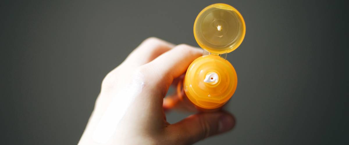 left hand holding a yellow, uncapped bottle of sunscreen
