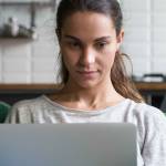 Horizontal photo focused mixed race woman sitting on couch at home working on laptop