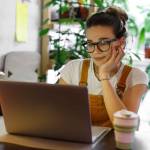 Young female gardener in glasses using laptop for remote work,