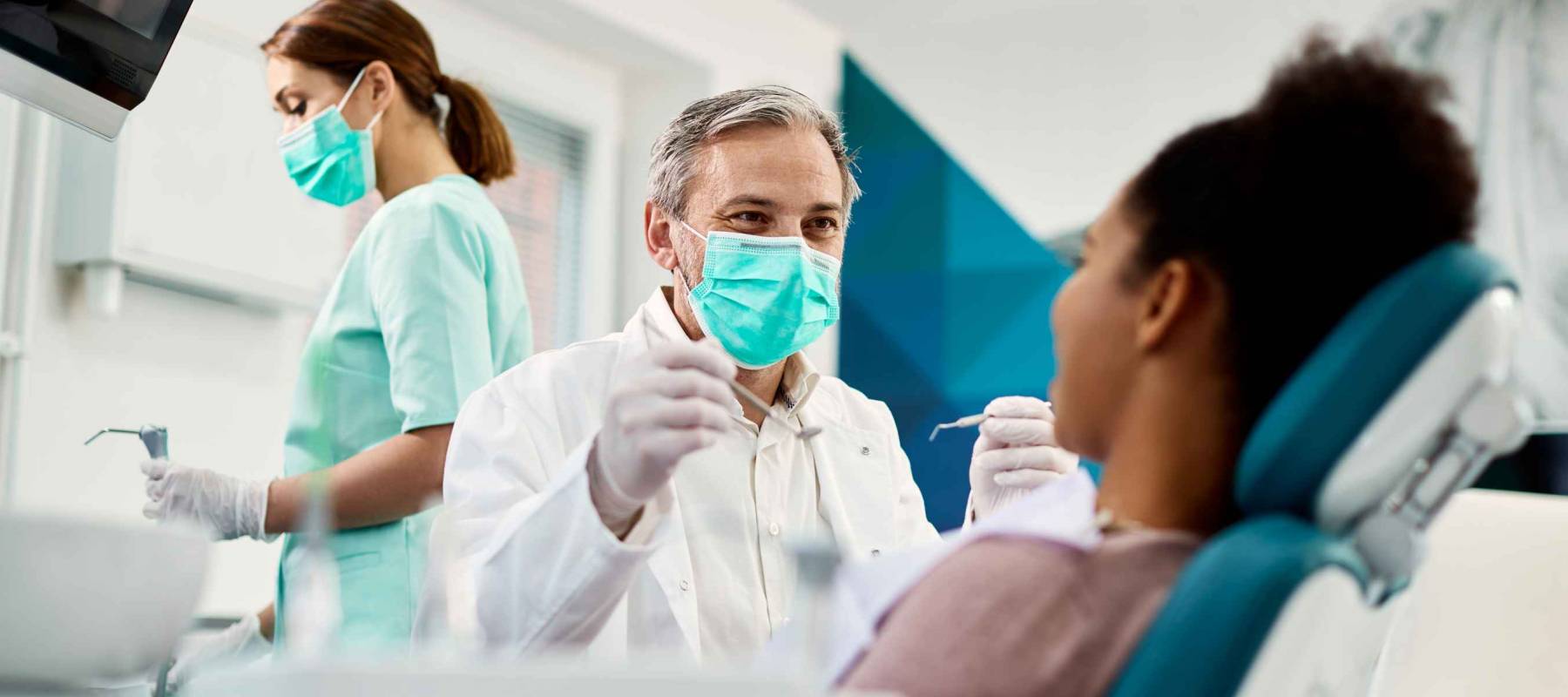 Smiling dentist communicating with African American woman while checking her teeth during dental procedure at dentist's office.